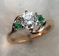 14Kt yellow gold 'Elizabeth' set with a 1.0ct round diamond and two side .12ct round emeralds.