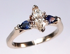 14Kt white gold 'Rebecca' Engagement Ring set with a .54ct marquise cut diamond and two .14ct pear shaped sapphires. Sapphires measure 4x3mm.