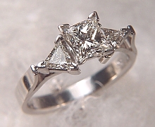 Platinum 'Susan' set with a 1.01ct princess cut diamond and two 4.5mm triangle cut diamonds on either side.